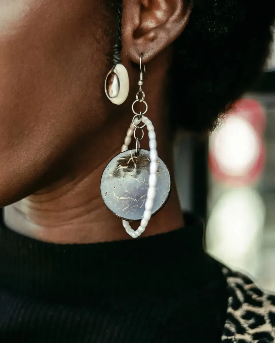 Close-up of a statement earring with a cowrie shell and a large shell disc hoop, worn with a black top.