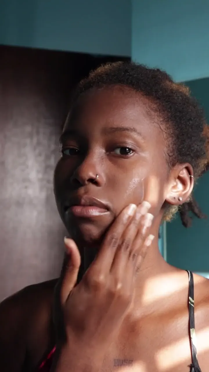 Sunlit UGC-style skincare video of a woman applying a glycolic youth renewal facial moisturizer and other products from the same line, smiling as she holds them to camera.