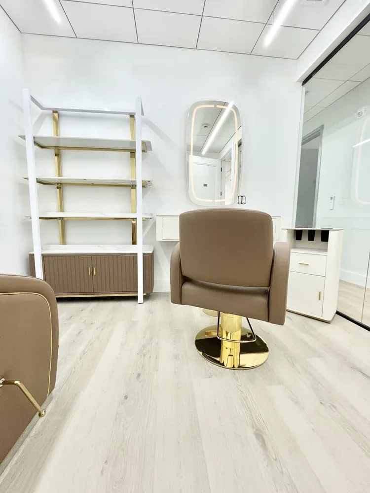 A white salon suite with gold and white open shelving, an arched lit mirror and a taupe styling chair with gold base.